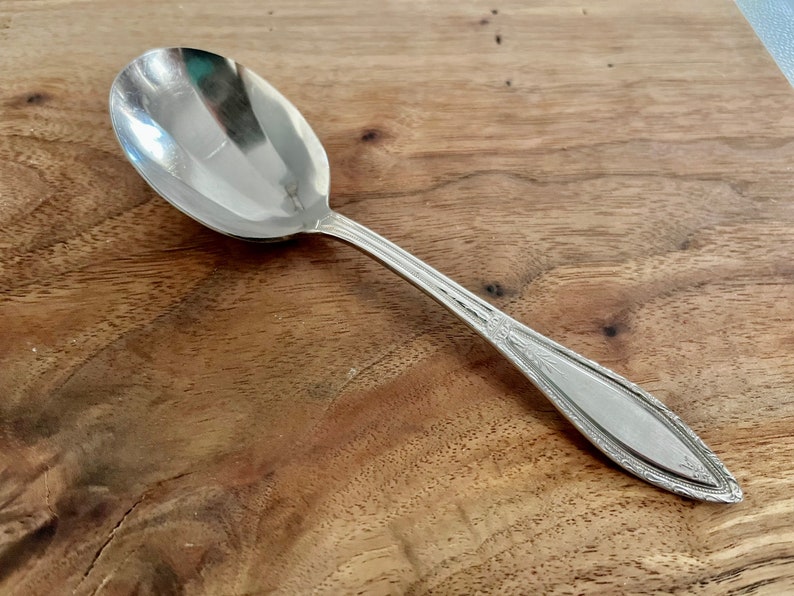 May include: A silver spoon with an ornate design on the handle. The spoon is on a wooden surface.