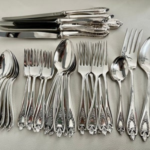 Puede incluir: Una colecci&oacute;n de cubiertos de plata pulida, que incluye cuchillos, tenedores y cucharas. La cuberter&iacute;a presenta detalles florales ornamentados en los mangos. La disposici&oacute;n incluye m&uacute;ltiples juegos de cubiertos, ideal para una cena formal.