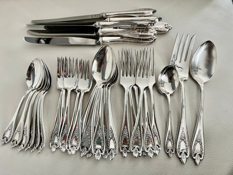 Puede incluir: Una colecci&oacute;n de cubiertos de plata pulida, que incluye cuchillos, tenedores y cucharas. La cuberter&iacute;a presenta detalles florales ornamentados en los mangos. La disposici&oacute;n incluye m&uacute;ltiples juegos de cubiertos, ideal para una cena formal.