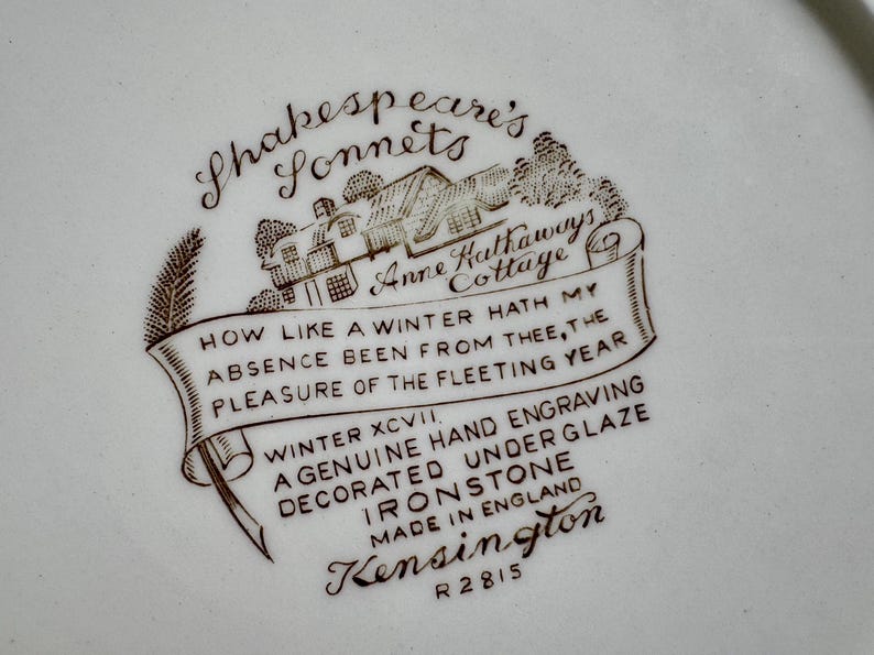 May include: A brown and white ceramic plate with a Shakespeare's Sonnets design. The design features a cottage with the text "Anne Hathaway's Cottage" and a quote from Shakespeare's Sonnet 97: "How like a winter hath my absence been from thee, the pleasure of the fleeting year." The plate is marked "Winter XCVII, A genuine hand engraving decorated underglaze Ironstone, Made in England, Kensington, R2815."