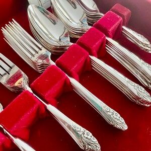May include: A set of silver-plated flatware, including forks and spoons, arranged in a red velvet-lined box. The silverware features a floral design on the handles. The set is ideal for formal dining occasions.
