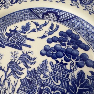 K&ouml;nnte beinhalten: Nahaufnahme eines blauen und wei&szlig;en Weidenmusters auf einem Keramikteller. Das Muster zeigt eine Pagode, einen Weidenbaum, V&ouml;gel und ein Boot.