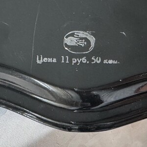 May include: Close-up of a black, glossy object with a rounded edge. The object has a silver emblem and text in a foreign language. The text is partially visible and appears to be a price.