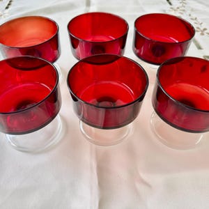 May include: Six clear glass dessert cups with red glass bases. The cups are arranged in two rows of three on a white tablecloth.