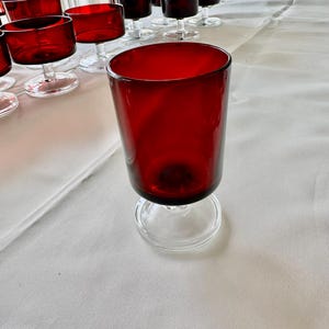 May include: A set of red glass goblets with clear glass stems and bases. The goblets are arranged on a white tablecloth.