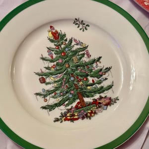 以下が含まれることがあります： 緑色の縁取りのある白いセラミック製のプレートには、赤、緑、金色のオーナメントが飾られたクリスマスツリーのデザインが施されています。ツリーはプレゼントとヤドリギの枝で囲まれています。
