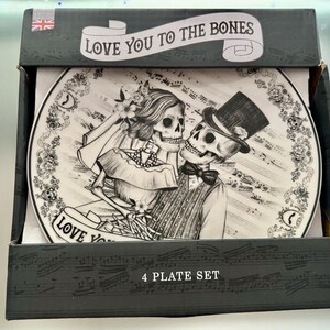 May include: A black and white plate set featuring a skeleton couple in wedding attire. The plate design includes musical notes and the phrase "Love You To The Bones." The box reads "4 PLATE SET" and has a Union Jack flag.
