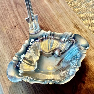 May include: A silver serving ladle with a fluted bowl and a decorative handle.