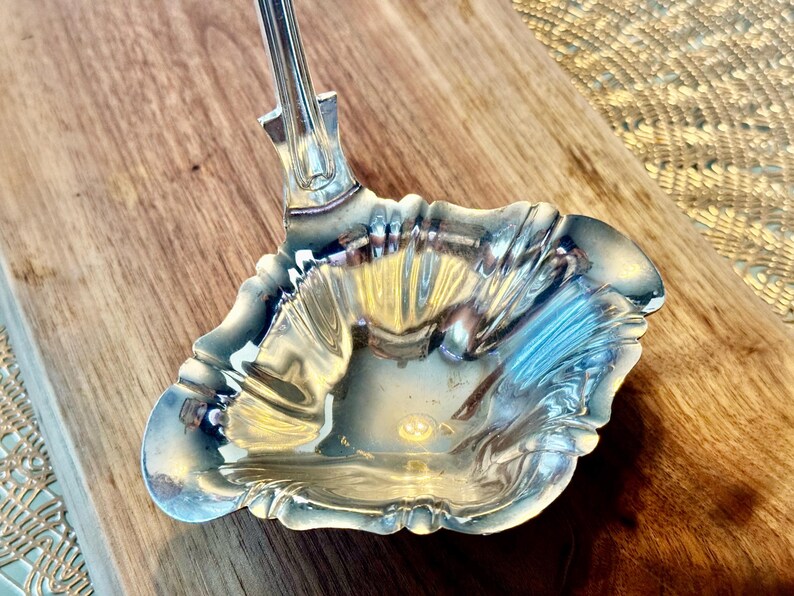 May include: A silver serving ladle with a fluted bowl and a decorative handle.