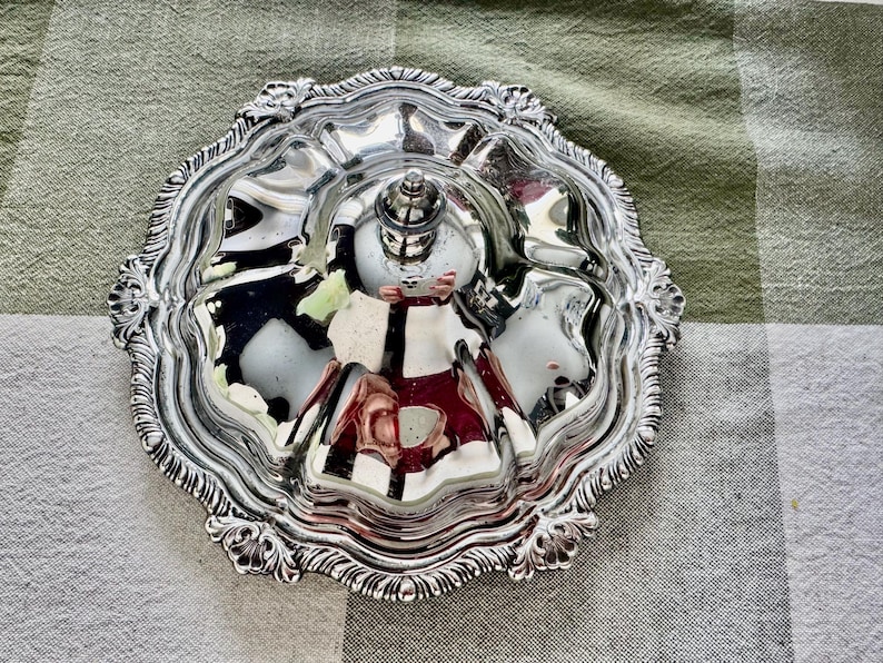 May include: Ornate silver serving dish with a central handle and multiple compartments. The dish has a decorative, scalloped edge and a reflective surface, perfect for serving appetizers or small portions.