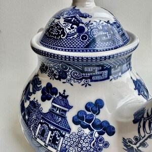 K&ouml;nnte beinhalten: Blaue und wei&szlig;e Porzellan-Teekanne mit traditionellem chinesischem Weidenmuster. Die Teekanne hat einen runden Korpus mit Deckel und Ausguss. Das Muster zeigt eine Pagode, B&auml;ume und Blumen.