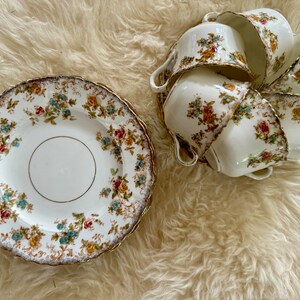 K&ouml;nnte beinhalten: Ein Set aus sechs Vintage-Teetassen und Untertassen mit einem floralen Muster in den Farben Rosa, Gelb, Blau und Gr&uuml;n. Die Tassen und Untertassen haben einen goldenen Rand.