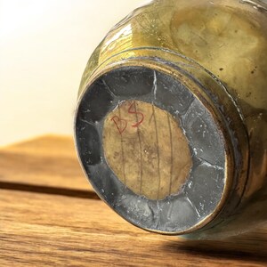 K&ouml;nnte beinhalten: Die Unterseite einer Messingvase mit einem runden Holzsockel. Der Sockel tr&auml;gt eine rote Inschrift mit der Aufschrift "BS".