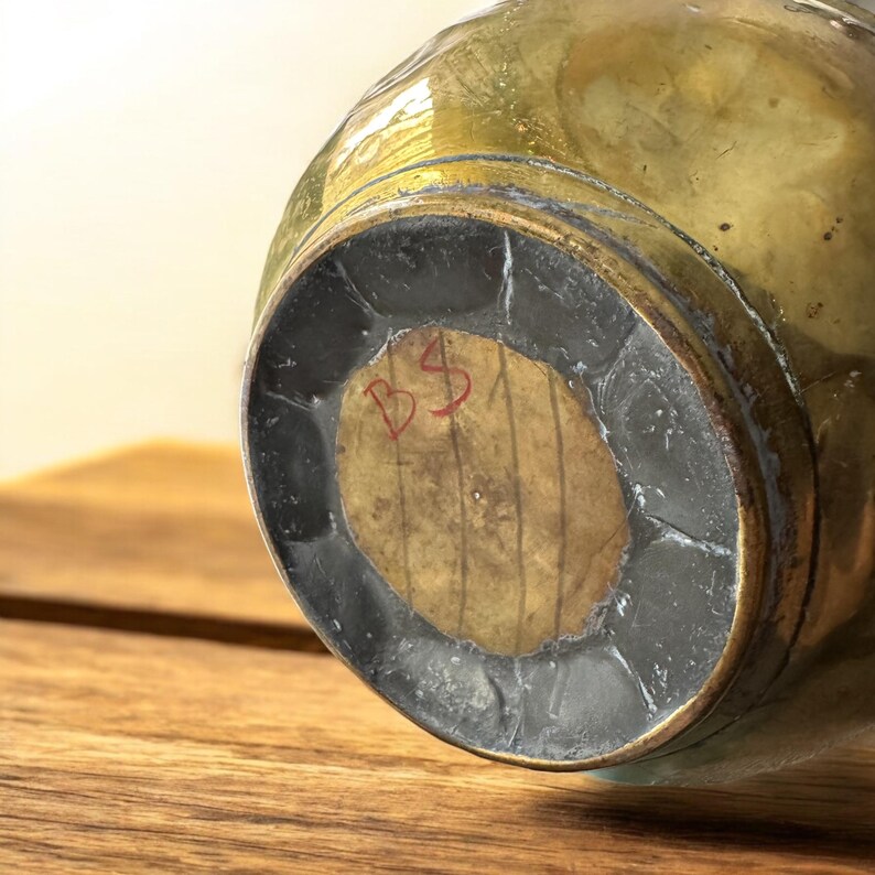 K&ouml;nnte beinhalten: Die Unterseite einer Messingvase mit einem runden Holzsockel. Der Sockel tr&auml;gt eine rote Inschrift mit der Aufschrift "BS".