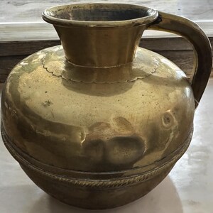 K&ouml;nnte beinhalten: Eine gro&szlig;e, runde, messingfarbene Kanne mit einem breiten Mund und einem Henkel. Die Kanne hat ein dekoratives Band um die Mitte und einen gewellten Rand oben.