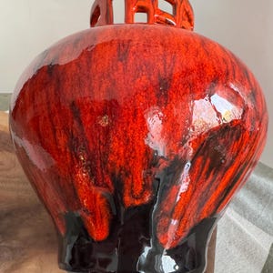 Puede incluir: Un jarr&oacute;n de cer&aacute;mica grande y redondo con un vibrante esmalte rojo y negro. El jarr&oacute;n tiene un dise&ntilde;o calado &uacute;nico en la parte superior y se apoya en peque&ntilde;os pies. El acabado brillante y las variaciones de color crean un efecto visual llamativo.