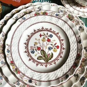 Op de afbeelding: Set van drie witte keramische dinerborden met een bruin, rood en blauw bloemenpatroon. De borden hebben een gegolfde rand en een geweven ontwerp.