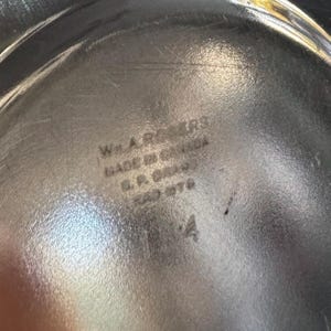Może przedstawiać: Srebrzysta metalowa powierzchnia z wytłoczonym znakiem producenta o treści Wm. A. ROGERS, MADE IN CANADA, A.1. BRAND oraz liczbą 184. Metalowa powierzchnia ma odblaskowe wykończenie z widocznymi odbiciami światła i drobnymi zarysowaniami.
