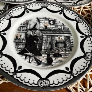 Może przedstawiać: Czarno-biały ceramiczny talerz z motywem Halloween, na kt&oacute;rym przedstawiono czarownicę mieszającą kociołek przed kominkiem. Talerz ma falisty brzeg i czarno-biały wz&oacute;r.