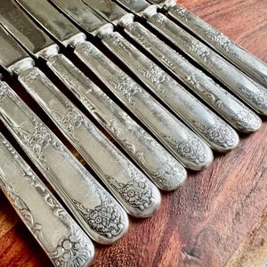 May include: A set of ten silver-plated dinner knives with ornate floral designs on the handles.