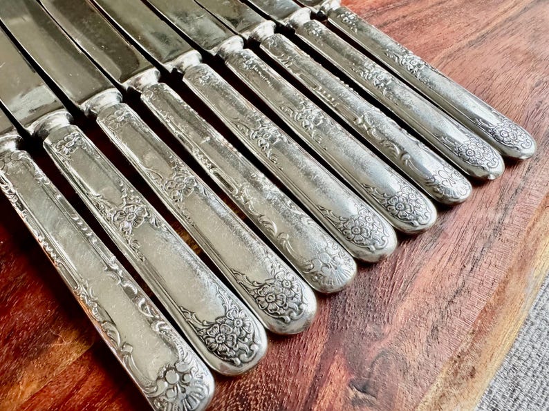 May include: A set of ten silver-plated dinner knives with ornate floral designs on the handles.