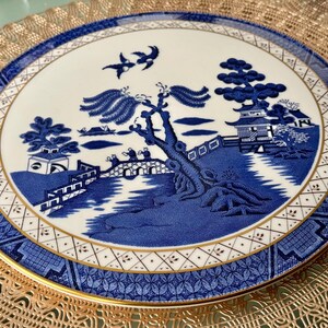 May include: A blue and white porcelain plate with a gold rim and a traditional Chinese design. The design features a bridge, a river, a tree, and a pagoda.