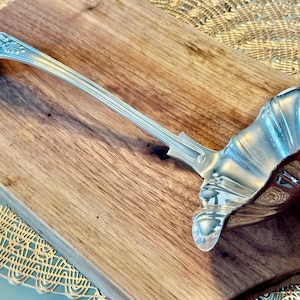 May include: A silver serving ladle with a decorative handle and a scalloped bowl.