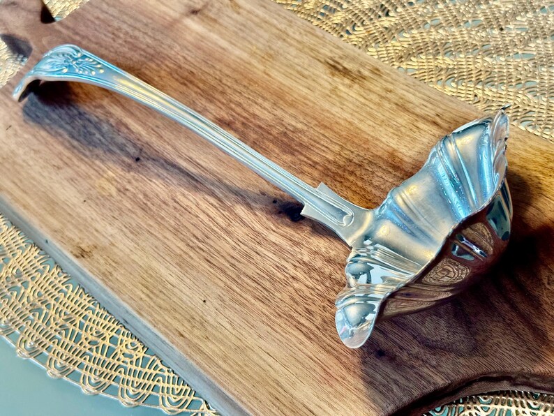 May include: A silver serving ladle with a decorative handle and a scalloped bowl.