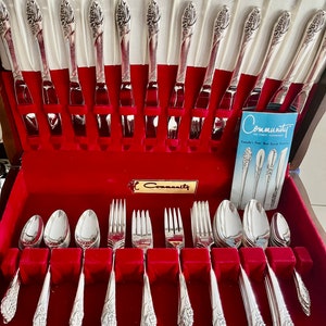 May include: A vintage silver Community silverware set displayed in a red velvet-lined case. The set includes forks, knives, and spoons with a decorative floral design on the handles. The case is open, revealing the neatly arranged utensils.