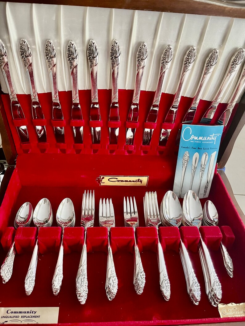 May include: A vintage silver Community silverware set displayed in a red velvet-lined case. The set includes forks, knives, and spoons with a decorative floral design on the handles. The case is open, revealing the neatly arranged utensils.