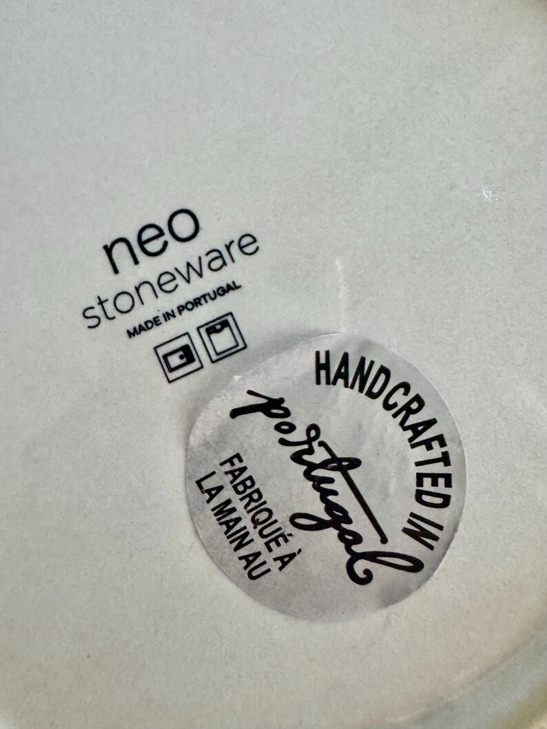 May include: A light-coloured stoneware surface featuring the black printed text neo stoneware MADE IN PORTUGAL with two square icons. A circular sticker is applied, reading HANDCRAFTED IN Portugal and FABRIQU&Eacute; &Agrave; LA MAIN AU in black text.