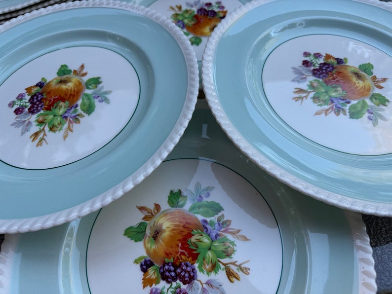 Puede incluir: Juego de cuatro platos de cer&aacute;mica vintage con un borde azul claro y un centro blanco con un dise&ntilde;o de frutas coloridas. Los platos tienen un borde de cuerda.