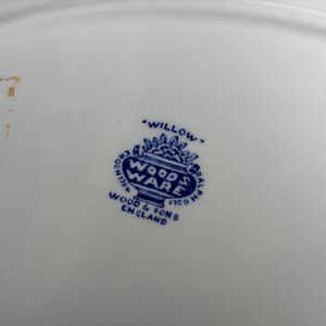 May include: A white ceramic plate base featuring a blue maker's mark in the center. The stamp displays the text "WILLOW," "WOOD & SONS," "ENGLAND," and "WOODS WARE" inside a decorative urn shape, with "ENOCH 1784" and "RALPH 1750" on the sides.
