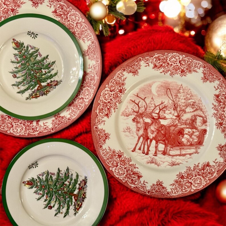 以下が含まれることがあります： 赤と緑の縁取りが施された白いセラミック製のプレート3枚。プレートには、クリスマスツリーとサンタクロースとトナカイのデザインが描かれています。