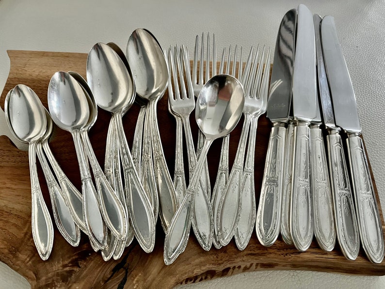 May include: A set of silver flatware, including spoons, forks, and knives, arranged on a wooden surface. The flatware has an ornate design and is in excellent condition.