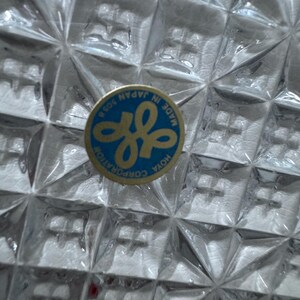May include: Close-up of a clear, textured glass object with a diamond pattern. A blue and gold sticker with the text "MADE IN JAPAN" and the Hoya Corporation logo is visible.