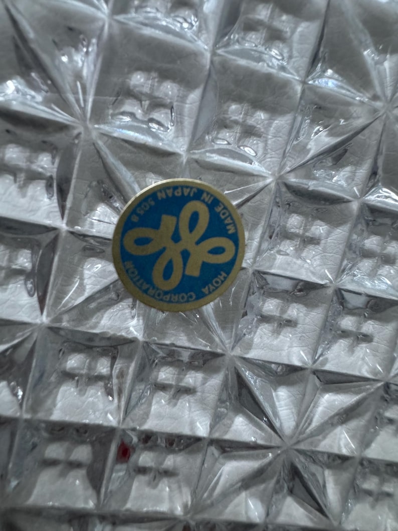 May include: Close-up of a clear, textured glass object with a diamond pattern. A blue and gold sticker with the text "MADE IN JAPAN" and the Hoya Corporation logo is visible.