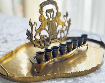May include: A vintage brass menorah with seven candle holders, set on an oval tray. The menorah features a decorative crest with lions. The brass has a warm, aged patina, and the tray has handles.