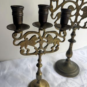 Pu&ograve; includere: Candelabro antico in ottone con un motivo decorativo a leoni. Il candelabro presenta pi&ugrave; portacandele e un design dettagliato e ornato. L'ottone ha una calda patina invecchiata, che ne aumenta il fascino vintage. La base &egrave; rotonda.