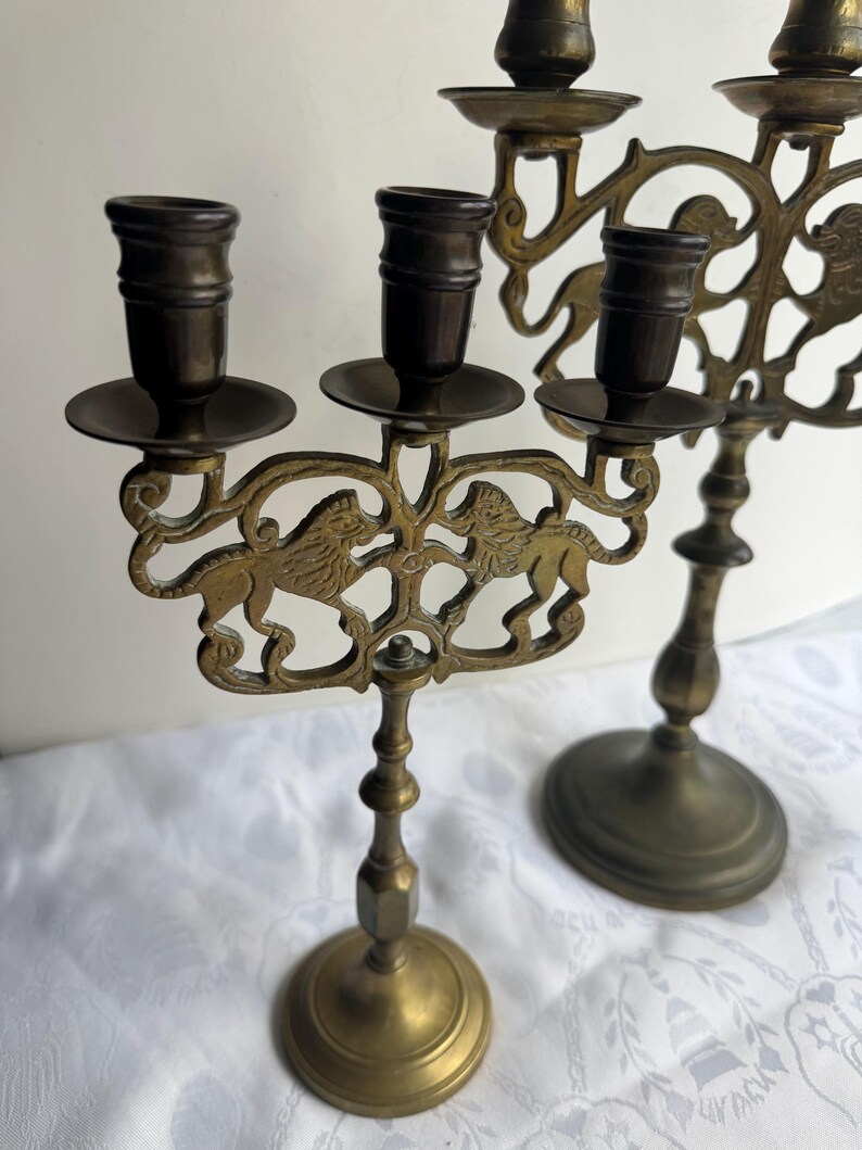 Pu&ograve; includere: Candelabro antico in ottone con un motivo decorativo a leoni. Il candelabro presenta pi&ugrave; portacandele e un design dettagliato e ornato. L'ottone ha una calda patina invecchiata, che ne aumenta il fascino vintage. La base &egrave; rotonda.