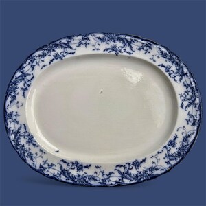 Puede incluir: Plato ovalado para servir con centro blanco y borde floral azul. El dise&ntilde;o azul presenta intrincados patrones de volutas y hojas. El plato tiene un borde festoneado y est&aacute; sobre un fondo azul.