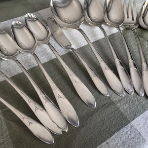 May include: A collection of stainless steel flatware including several spoons, a butter knife, and a serving fork. Each piece features a polished finish and a decorative etched pattern on the handle, showcasing a consistent design across the set.