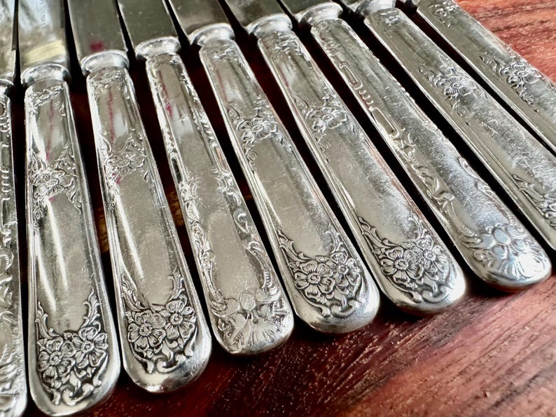 May include: A set of ten silver-plated dinner knives with ornate floral designs on the handles.