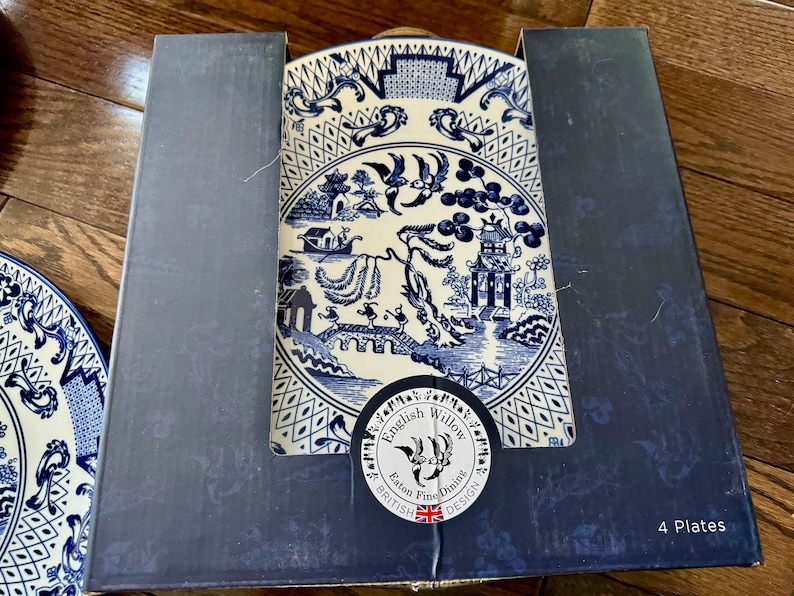 K&ouml;nnte beinhalten: Ein Set von vier English Willow Feinteller in einer Box. Die Teller zeigen ein blau-wei&szlig;es Design mit einem klassischen Willow-Muster. Die Box ist dunkelblau und zeigt den Markennamen und die Anzahl der Teller.
