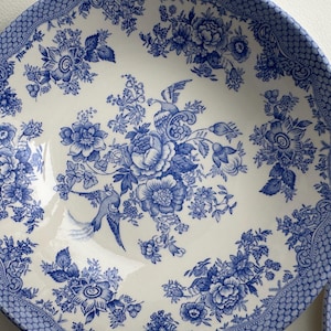 K&ouml;nnte beinhalten: Eine wei&szlig;e Keramiksch&uuml;ssel mit einem blauen und wei&szlig;en Blumenmuster. Die Sch&uuml;ssel zeigt ein sich wiederholendes Muster aus Blumen, Bl&auml;ttern und V&ouml;geln. Die Sch&uuml;ssel ist perfekt zum Servieren von Salaten, Obst oder anderen Gerichten.