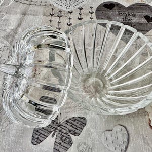 May include: A clear glass bowl with a matching lid, both featuring a ribbed, pumpkin-like design. The lid includes a small, pointed handle at the top. The glass is transparent with vertical ridges that create a faceted appearance throughout the piece.