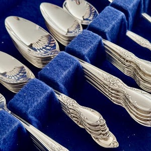 K&ouml;nnte beinhalten: Ein Set silbernes Besteck in einem blauen Samt-Etui. Das Besteck umfasst Gabeln, Messer und L&ouml;ffel.