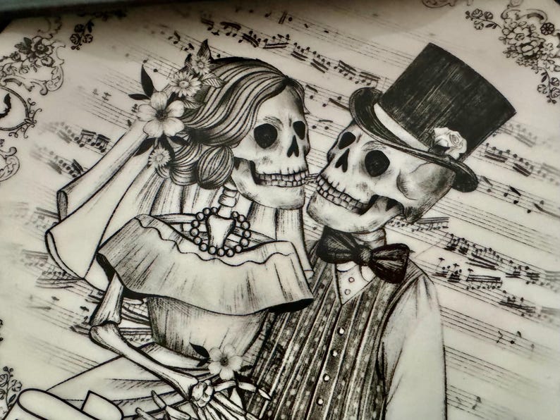 May include: Black and white illustration of a skeleton couple, the bride wearing a veil and flowers, the groom in a top hat and bow tie. The background features musical notes and floral accents, creating a romantic, yet gothic theme.