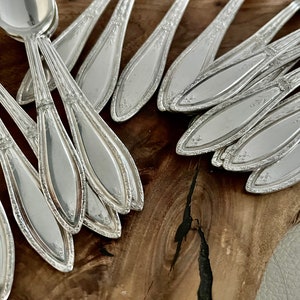May include: A close-up of a pile of silver spoons with ornate designs on the handles. The spoons are arranged in a fan shape, with the bowls facing up.