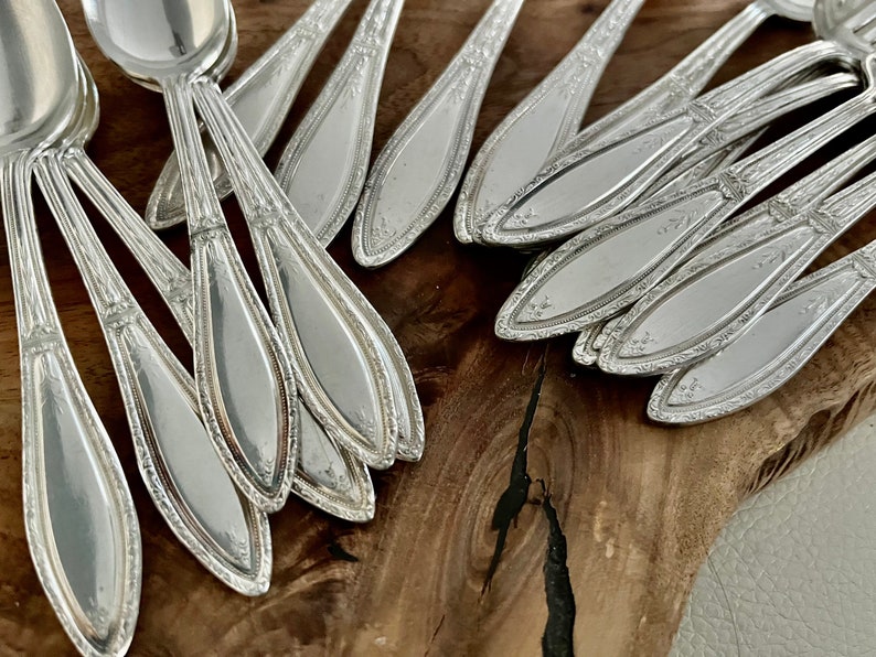 May include: A close-up of a pile of silver spoons with ornate designs on the handles. The spoons are arranged in a fan shape, with the bowls facing up.